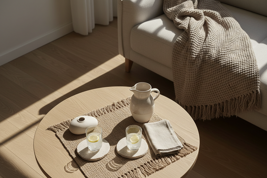 Minimalist living room styled for summer entertaining with stone coasters, woven place mat, and linen throw on a neutral coffee table