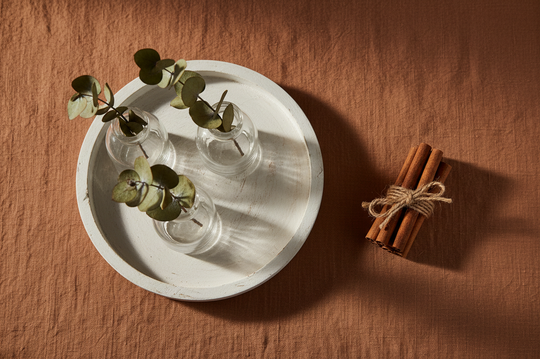 Thanksgiving hostess gift flat lay with a whitewash wood candle tray, crystal bud vases, dried eucalyptus, and cinnamon sticks on linen